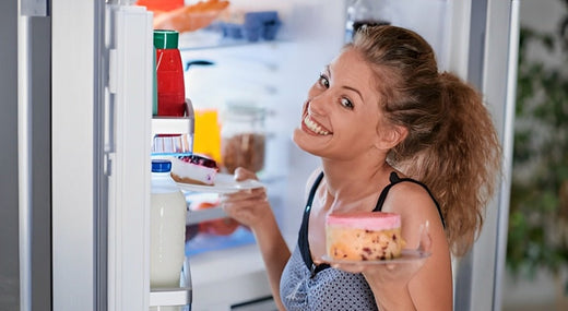 A lady smiles and pulls a cheesecake out of the fridge