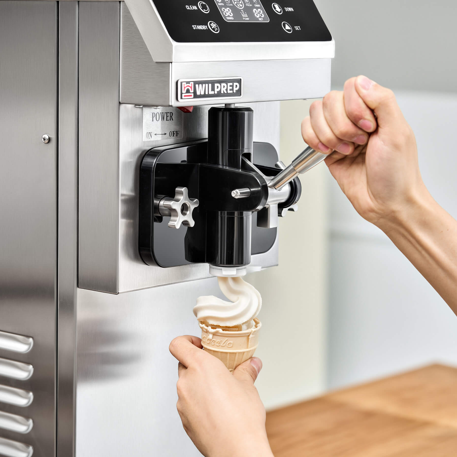 Commercial ice cream machine with a single flavor dispenser, digital control panel, and cone rack. The machine is constructed from stainless steel and there are three flavored ice cream cones depicted above it.