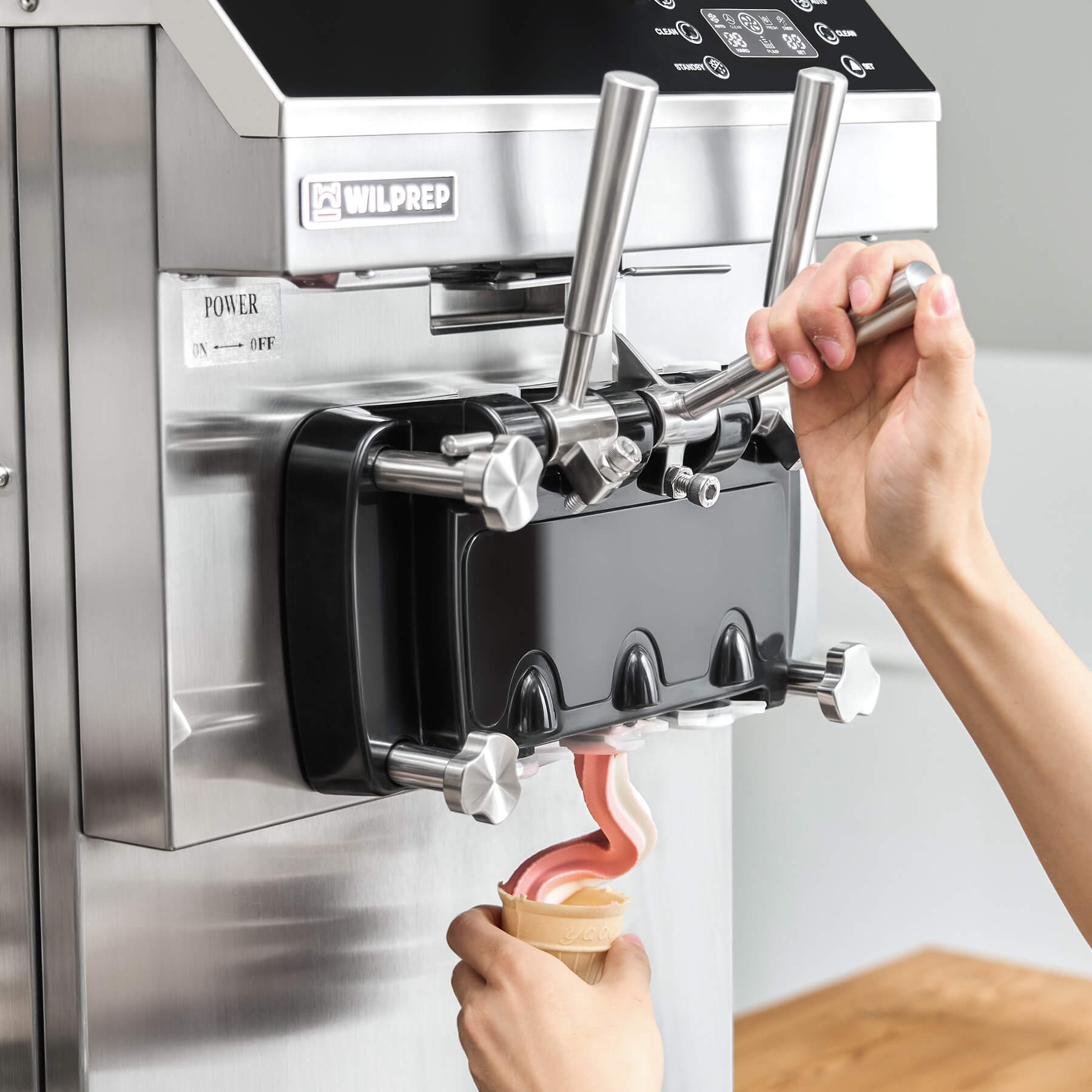 Commercial ice cream machine with three flavor dispensers, digital control panel, and a cone rack. The machine is constructed of stainless steel and is pictured with examples of ice cream cones.